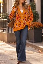 Load image into Gallery viewer, Model wearing a golden-orange V-neck button-front cardigan with multicolored animal print and long sleeves.
